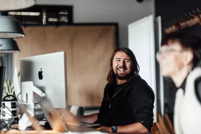 Ein Mitarbeiter der Werbeagentur BICEPS arbeitet an einem iMac im Büro, während eine Kollegin im Vordergrund unscharf zu sehen ist.