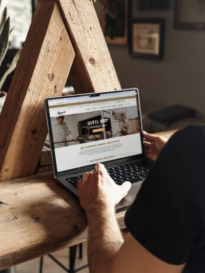 Mitarbeiter der Werbeagentur BICEPS arbeitet an einem Laptop mit geöffneter Website der Holzofenbäckerei Ripken, sitzend an einem Holztisch in gemütlicher Umgebung.