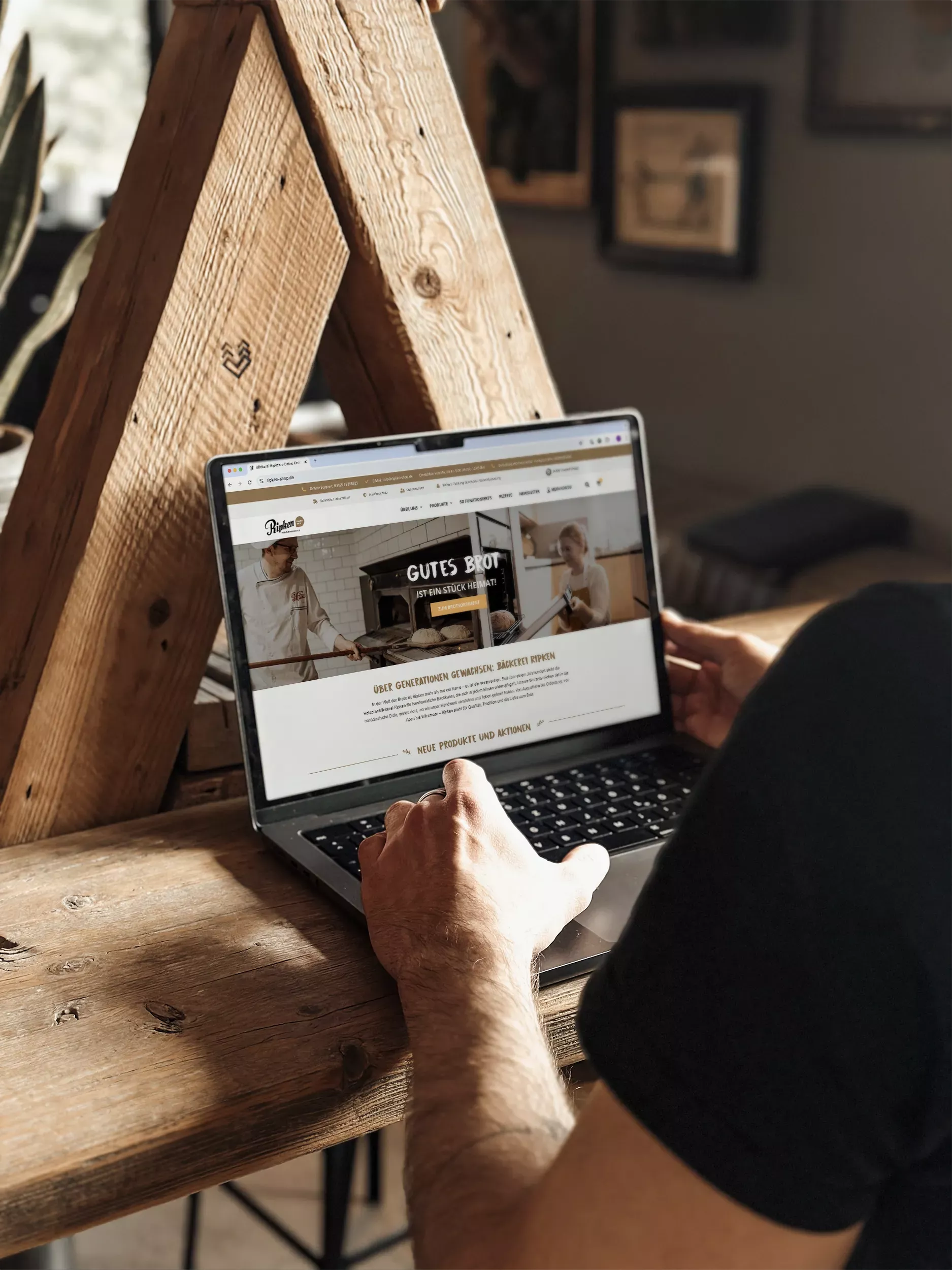 Mitarbeiter der Werbeagentur BICEPS arbeitet an einem Laptop mit geöffneter Website der Holzofenbäckerei Ripken, sitzend an einem Holztisch in gemütlicher Umgebung.