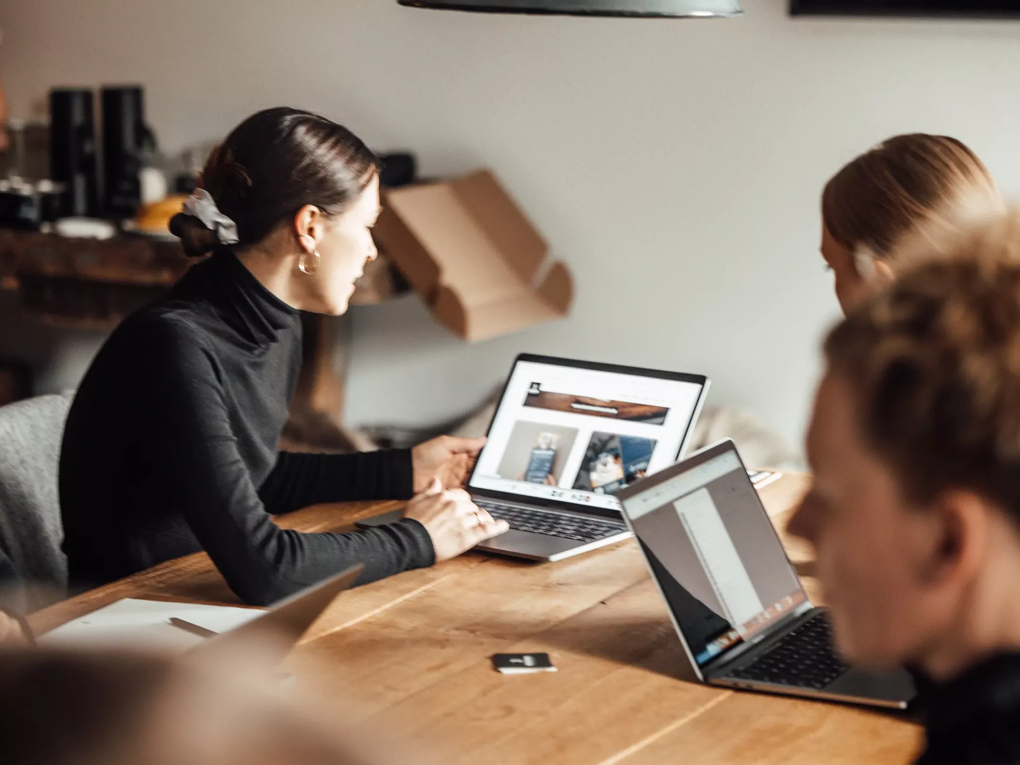 Teammeeting in der Werbeagentur BICEPS: Zwei Personen sitzen an einem Tisch und betrachten gemeinsam eine Website auf einem Laptop, während weitere Kolleg:innen mitarbeiten.