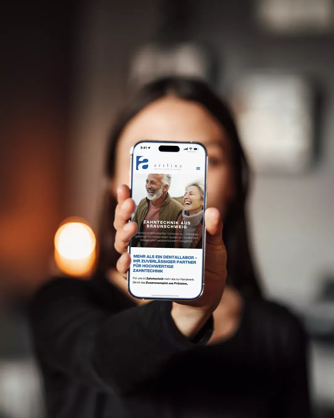 Person hält ein Smartphone in der Hand, auf dem die mobil optimierte Website des Art-Line Dentallabors mit Startseite zu moderner Zahntechnik aus Braunschweig zu sehen ist.