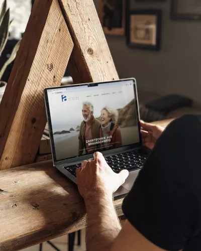 Eine Person arbeitet an einem Laptop, auf dem die Website des Art-Line Dentallabors mit einer Startseite zu moderner Zahntechnik aus Braunschweig geöffnet ist.
