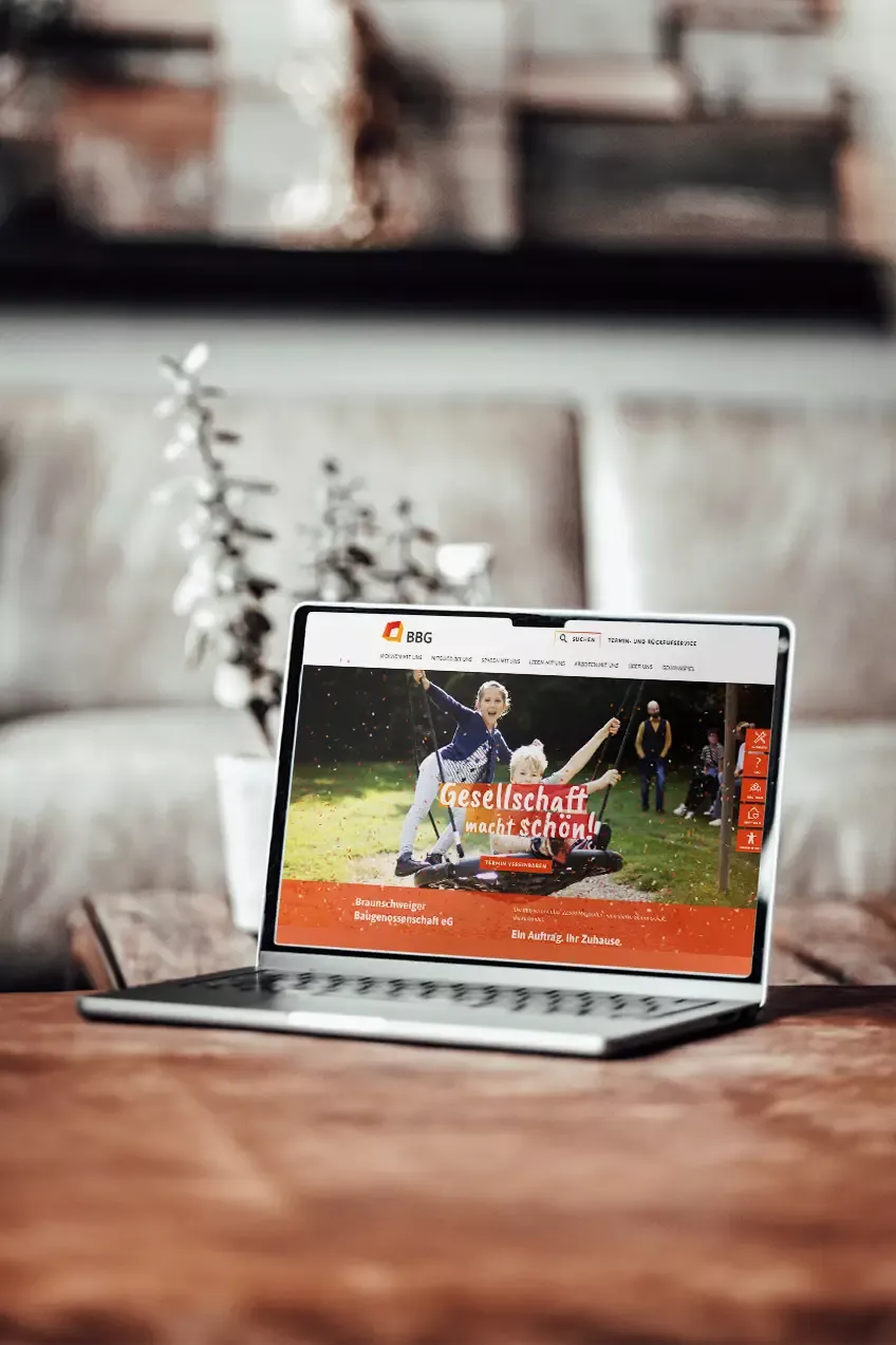 Startseite der neu gestalteten Website der Braunschweiger Baugenossenschaft auf einem iMac in modernem Büroambiente, mit Barrierefreiheit-Funktionen und Fokus auf Gemeinschaft.