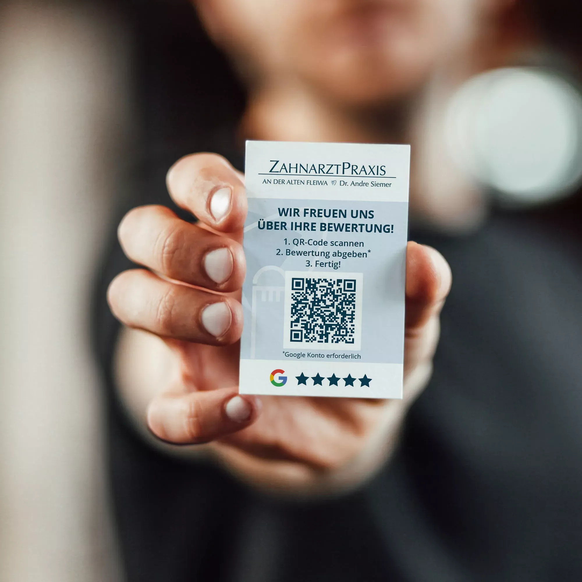 Eine Hand hält eine kleine Bewertungskarte der „Zahnarztpraxis an der Alten Fleiwa“. Auf der Karte befinden sich das Praxislogo, ein QR-Code zur Google-Bewertung, eine kurze Anleitung zur Bewertungsabgabe und fünf Bewertungssterne. Das Design ist klar, freundlich und modern gestaltet.