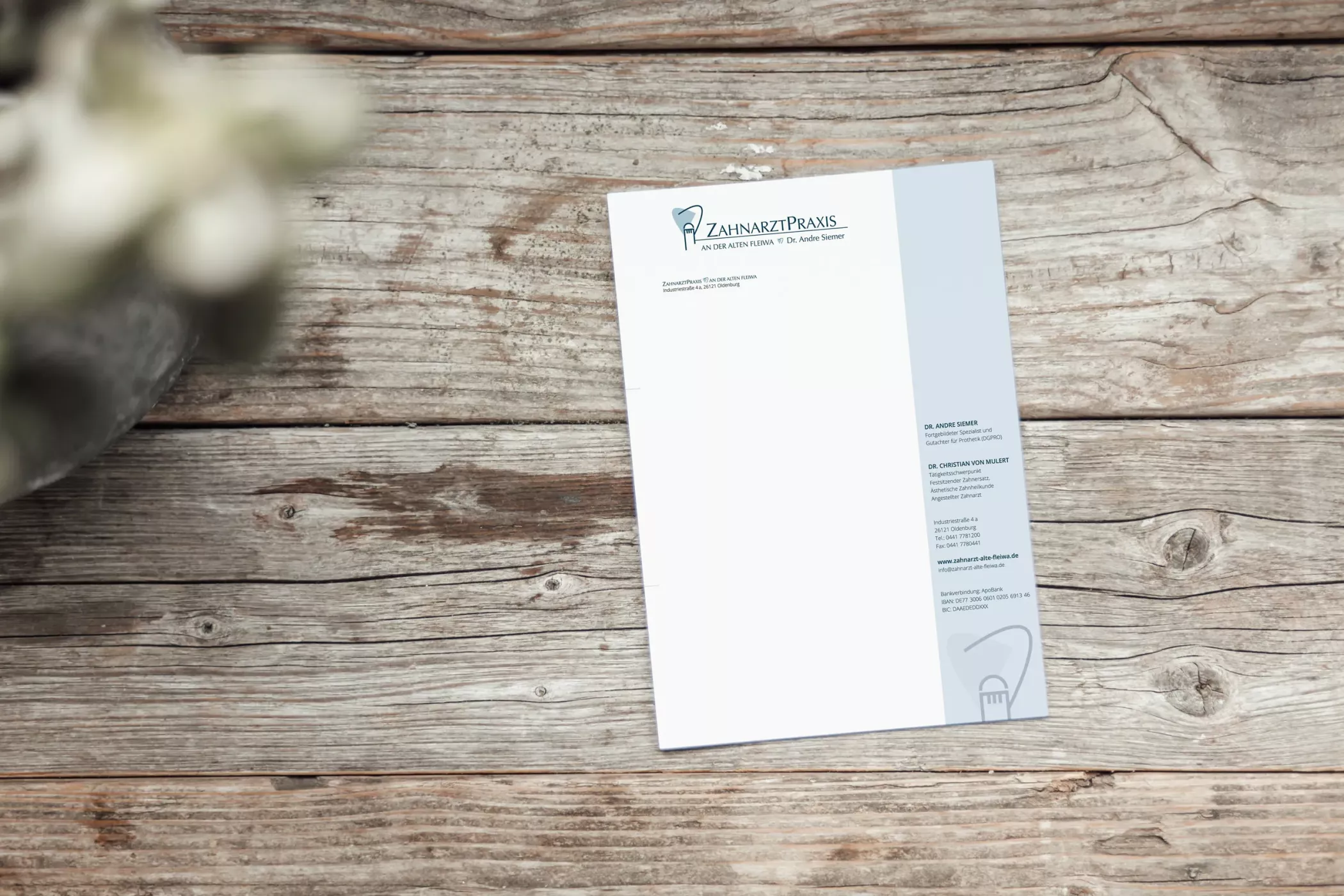 Ein Briefpapier der „Zahnarztpraxis an der Alten Fleiwa“ in Hannover liegt auf einem rustikalen Holztisch. Oben links ist das Praxislogo mit stilisierter Darstellung der Alten Fleiwa zu sehen, rechts befinden sich Kontaktinformationen der Praxis. Das Design ist modern, klar und hochwertig gestaltet.