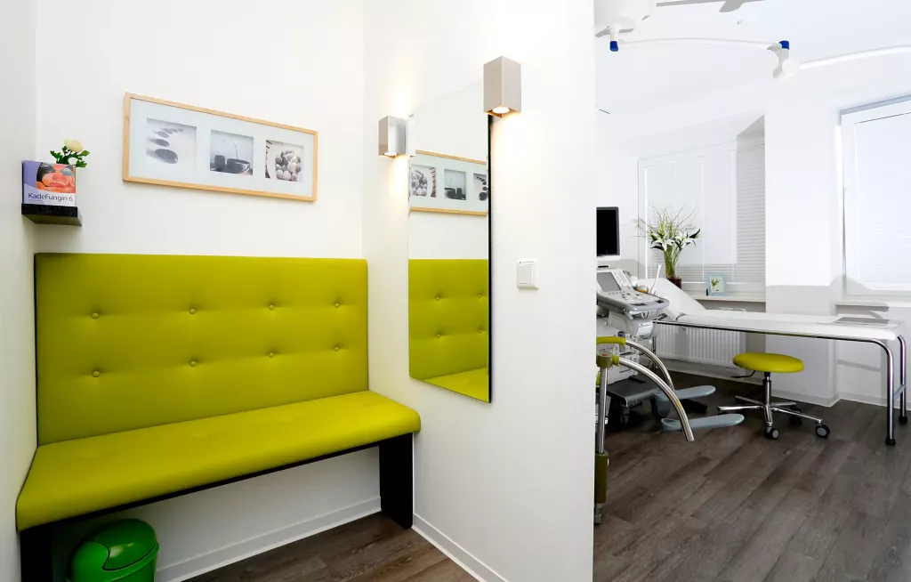 Vor einem Wartezimmer ist ein kleiner Wartebereich mit einer grünen Sitzgelegenheit.