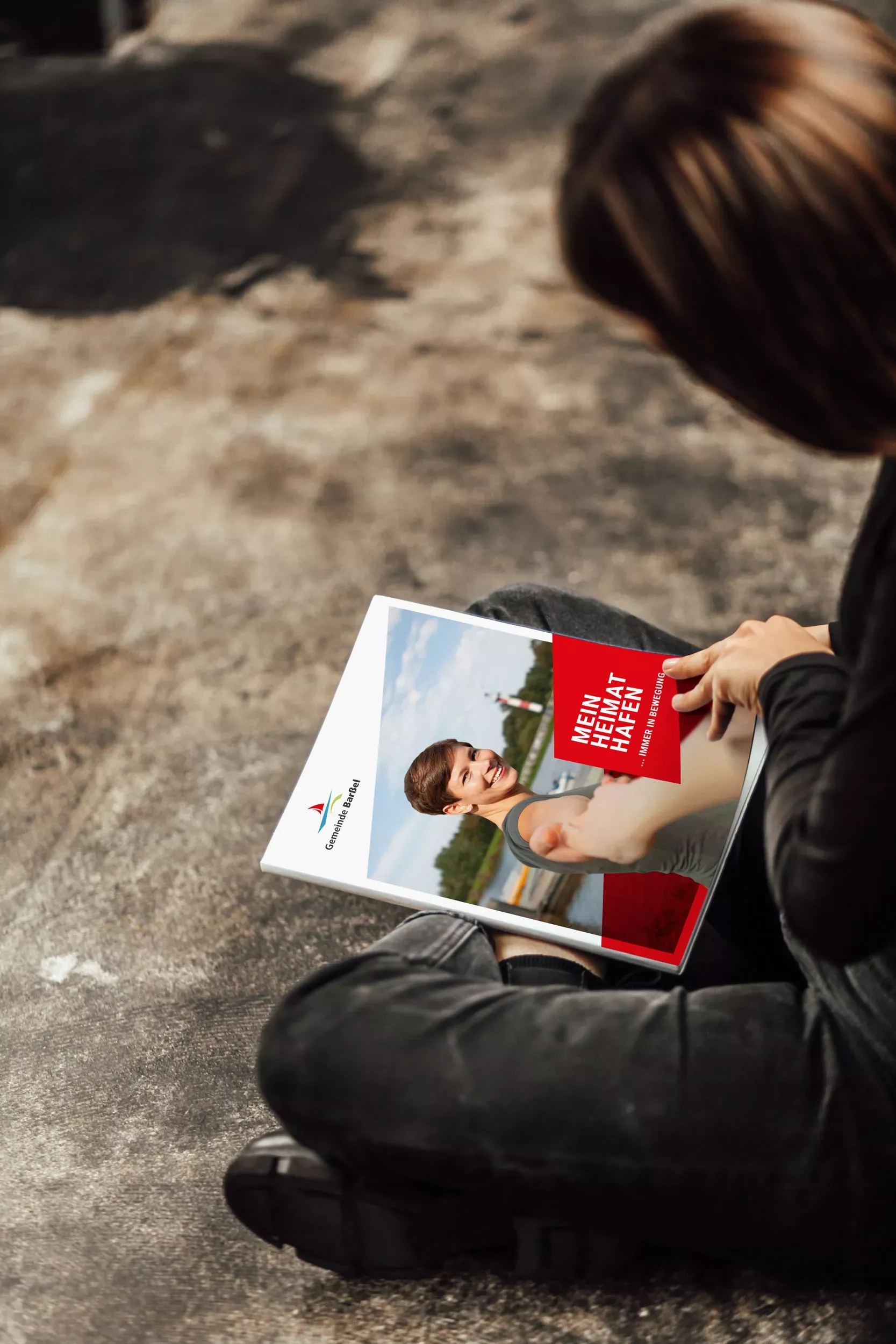 Person hält eine Broschüre der Gemeinde Barßel mit Bildmotiv und Informationen zur Gemeinde und ihren Angeboten in der Hand.