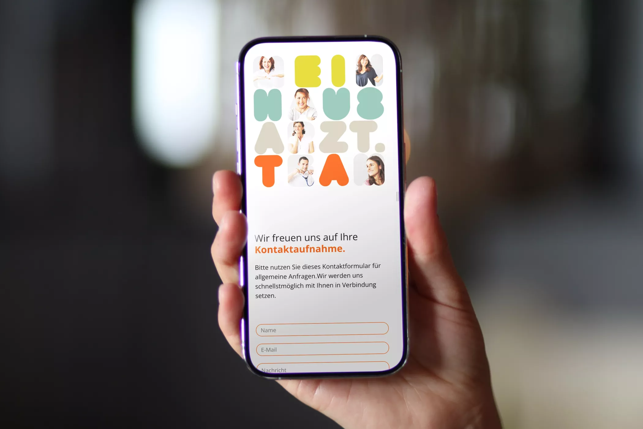Eine Hand hält ein Smartphone, das die Kontaktseite der Website von meinhausarzt.team zeigt. Auf dem Bildschirm sind die bunten Buchstaben „MEINHAUSARZT.TEAM“ mit Fotos der Teammitglieder zu sehen. Darunter befindet sich ein Kontaktformular mit den Feldern Name, E-Mail und Nachricht. Das Design wirkt freundlich, modern und einladend.