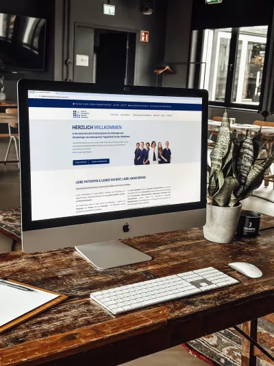 Ein iMac auf einem Holztisch zeigt die Website der