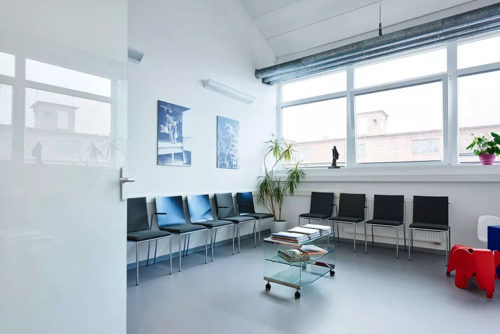 Eine Tür ist geöffnet und führt zu einem Wartezimmer mit vielen Stühlen.