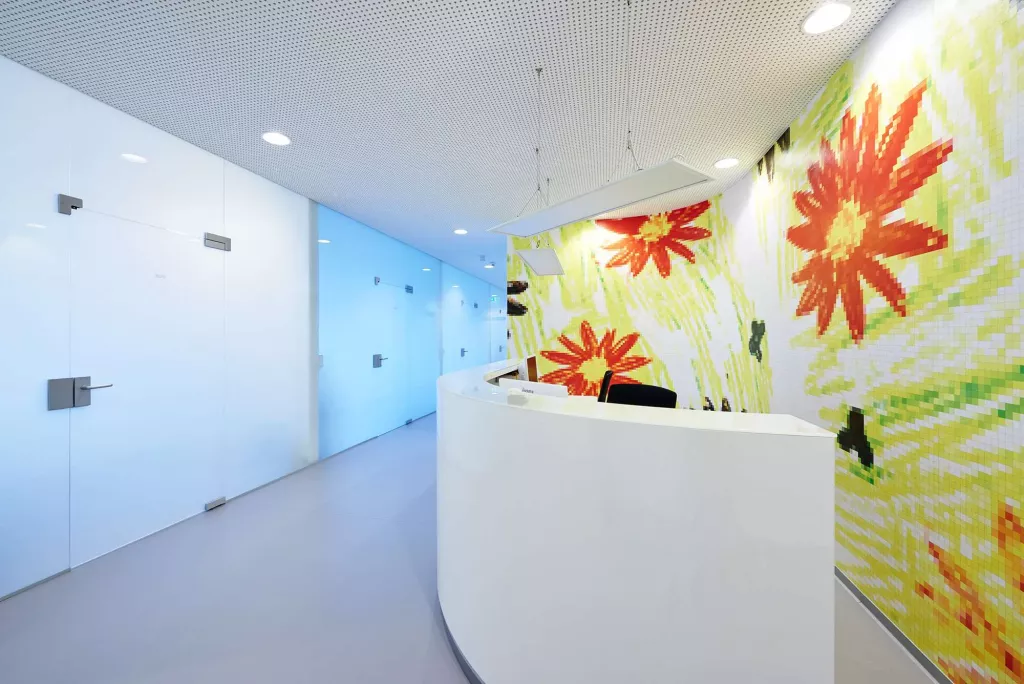 Ein weißer Tresen steht in einer Arztpraxis vor einer bunten Wand mit Blumen.