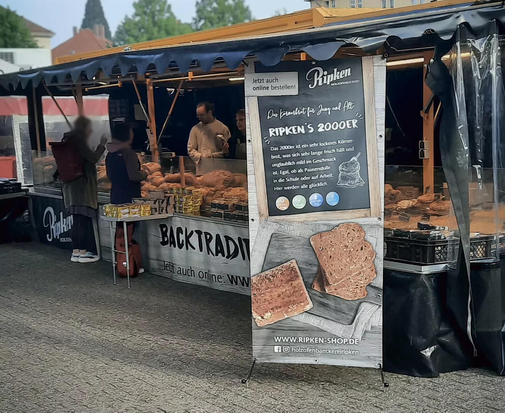 Kund:innen kaufen an einem Wochenmarktstand Backwaren ein.