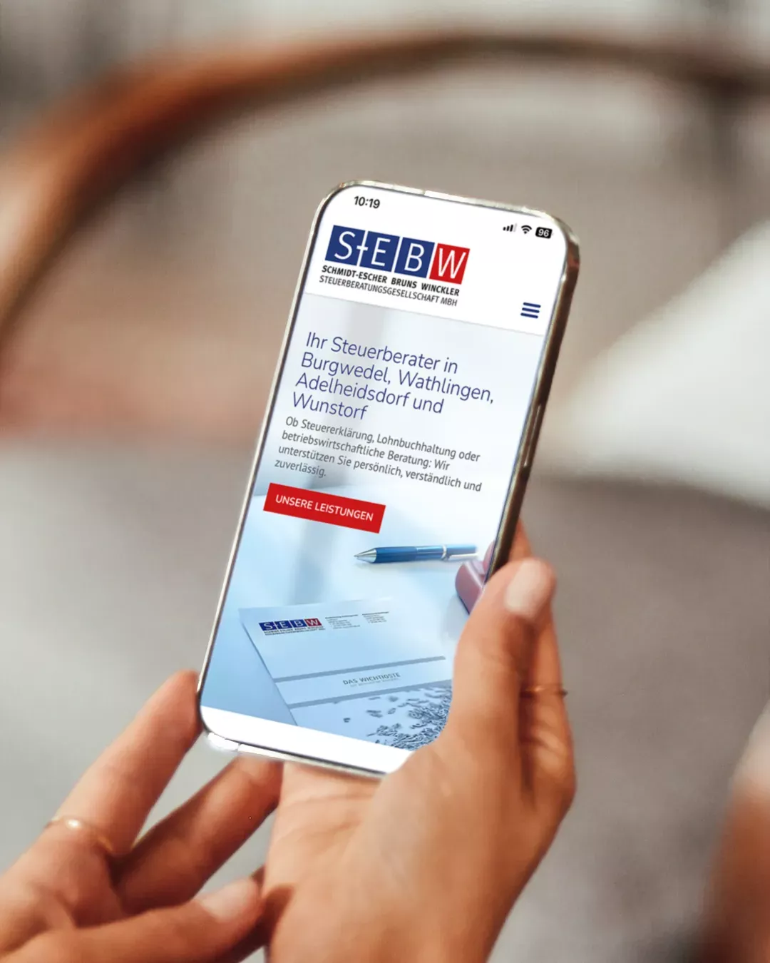 Person hält ein Smartphone, auf dem die mobil optimierte Website der SEBW Steuerberater mit Startseite und Leistungsübersicht angezeigt wird.