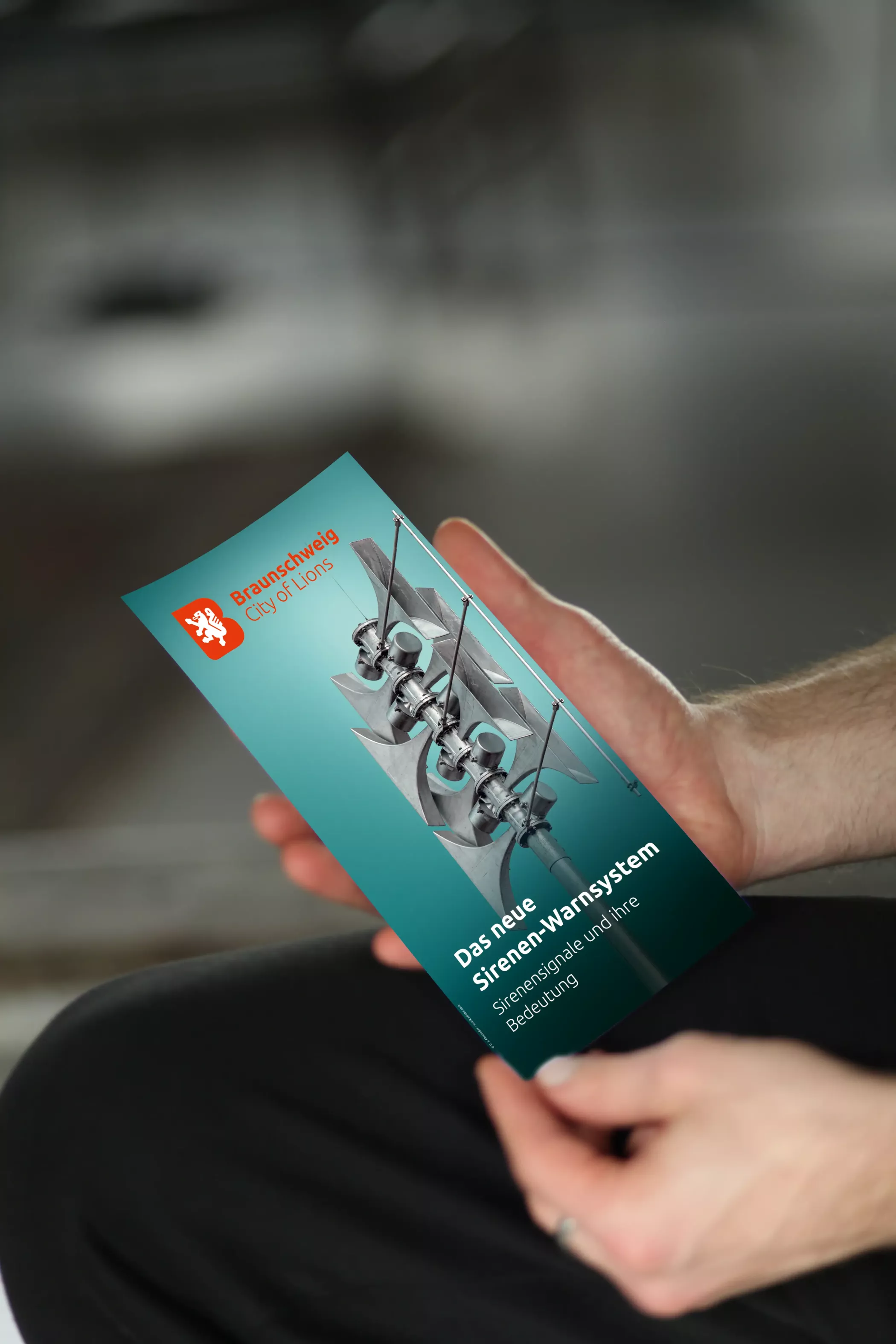 Eine Person hält einen Flyer zum neuen Sirenenwarnsystem in Braunschweig mit Informationen zu Sirenensignalen und deren Bedeutung.